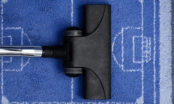 Ssawka odkurzacza na niebieskim dywanie w kształcie boiska do piłki nożnej